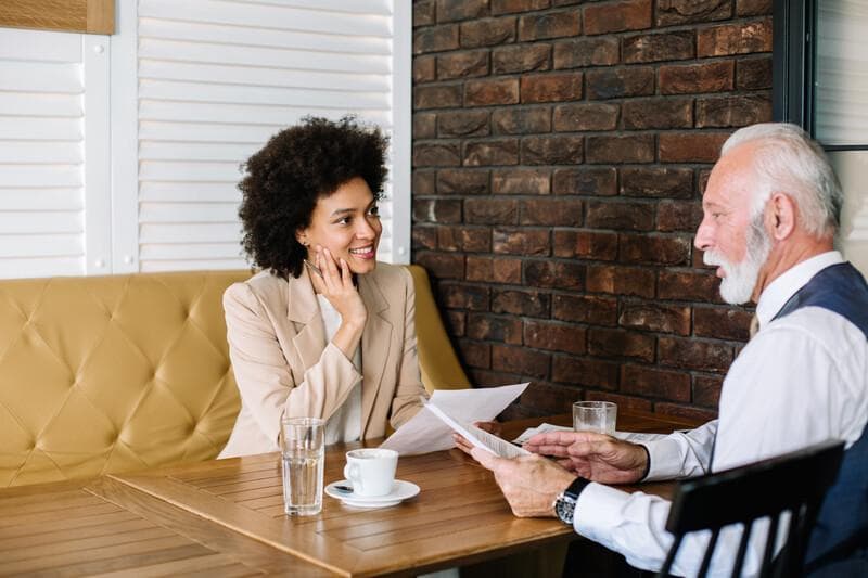 Young mixed race businesswoman and senior businessman brainstorming about new project while sitting in a coffee shop.